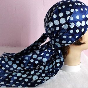 May include: A navy blue head wrap with a white polka dot pattern. The head wrap is tied at the back, with long flowing fabric. The head wrap is on a mannequin head.