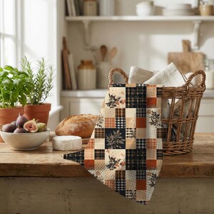 May include: A rectangular kitchen towel featuring a patchwork design of alternating squares in black, white, and burnt orange. The pattern includes solid colors, gingham checks, and botanical illustrations of leaves and flowers on a textured fabric.