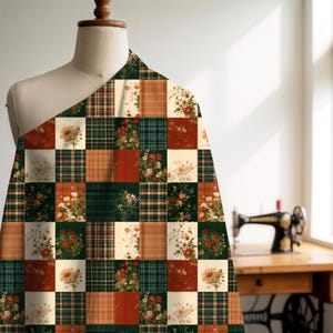 May include: A fabric swatch draped over a mannequin featuring a patchwork grid pattern. The design alternates between squares of dark green and orange plaid, solid rust red, and cream-colored squares decorated with floral illustrations.
