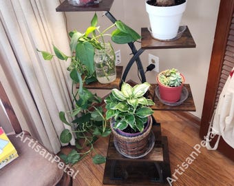 May include: A multi-tiered plant stand with various potted plants. The stand has dark wooden shelves and a black metal frame. Plants include a fern in a red pot, a ponytail palm in a white pot, and other green plants in decorative pots. The stand is indoors.