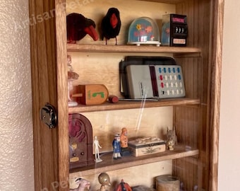 May include: A wooden display cabinet with a glass front, showcasing various vintage collectibles. The cabinet features multiple shelves holding items like figurines, a snow globe, and a vintage radio. The cabinet is made of light brown wood.