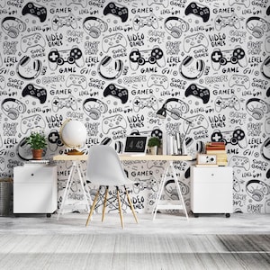 May include: Black and white gamer-themed wallpaper featuring hand-drawn illustrations of game controllers, headphones, and text like "Video Games On" and "Just Level Up!". The wallpaper is used as a backdrop for a desk and office setup.