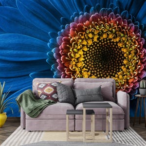 May include: A vibrant floral wall mural featuring a large blue flower with a multi-colored center. A mauve sofa with decorative pillows and a green throw is in front of the mural. A yellow pot with a plant is on the left.