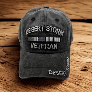 Puede incluir: Gorra de béisbol gris carbón con las palabras "DESERT STORM VETERAN" bordadas en la parte delantera. La gorra tiene una visera curva y un aspecto desgastado. El texto "DESERT STORM" también está bordado en el lateral.