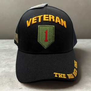 May include: Black baseball cap with the word "VETERAN" embroidered in gold. The cap features a patch with a red "1" and the words "THE BIG RED ONE" in gold.