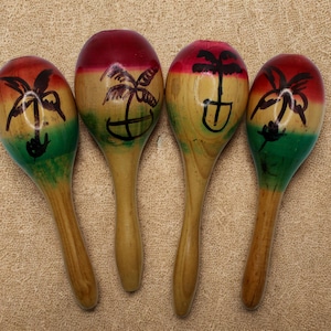 May include: Four wooden maracas arranged in a row, each featuring a rounded head painted with horizontal bands of red, yellow, and green. Each maraca head displays a hand-painted black palm tree silhouette, while the handles remain natural wood.
