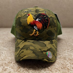 May include: A camouflage baseball cap with a detailed embroidered rooster design. The rooster features yellow, red, and black colors. The cap has a green mesh back and a curved brim. The overall color scheme is olive green and brown.