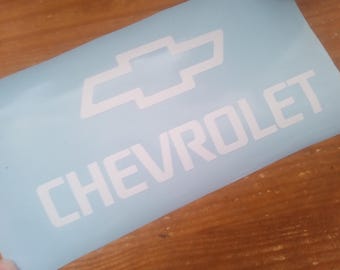 May include: A light blue decal featuring the white Chevrolet logo and the word "CHEVROLET" in a bold, sans-serif font. The decal is rectangular and appears to be made of vinyl.