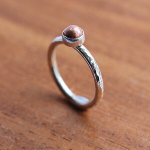 May include: A hammered silver band ring with a copper sphere on top.