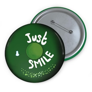 May include: Green button with white text that says "Just Smile" and a green circle in the middle. The back of the button is silver with a green border.