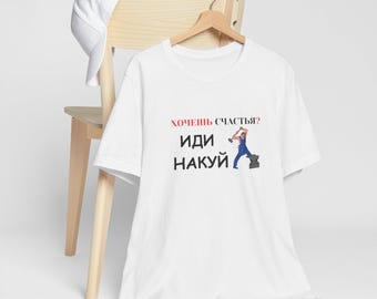 May include: White t-shirt with the Russian text "Want happiness? Go..." and a graphic of a person hammering an anvil. A white baseball cap rests on a wooden chair behind the shirt.