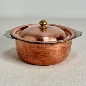 May include: A small copper pot with a lid and two handles. The pot has a gold knob on the lid.