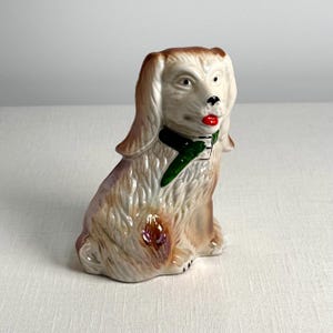 May include: A ceramic figurine of a brown and white dog with green and black collar and red lips. The dog is sitting with its head turned to the right.