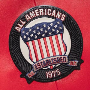 Back embroidery detail of men’s red vintage aviator leather bomber jacket showing bold aviation patch artwork carefully stitched onto genuine sheepskin leather. The oversized bomber silhouette with ribbed waistband and cuffs creates a timeless retro streetwear style that stands out in modern men’s fashion.