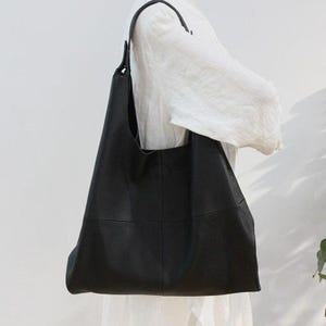 Minimalist black leather hobo tote bag with oversized slouchy silhouette displayed against a soft neutral background. Elegant genuine leather shoulder bag featuring a soft pebbled texture, spacious large capacity interior, modern quiet luxury aesthetic, chic everyday handbag for women, stylish carryall tote purse, designer inspired leather bag, casual minimalist fashion accessory, trendy oversized shoulder tote, laptop friendly work bag, handmade leather purse, capsule wardrobe essential