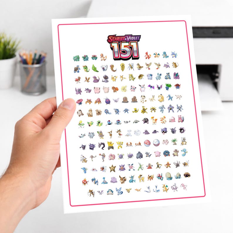 May include: A white print featuring the text "Scarlet & Violet 151" above a grid of colorful cartoon characters. The print has a pink border and is held by a person's hand.