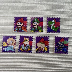 Puede incluir: Siete pegatinas rectangulares coloridas con personajes de la serie de videojuegos Super Mario. Las pegatinas tienen un borde morado y representan a Mario, Luigi, Yoshi, Rosalina, Fox, Bowser y un Shy Guy.