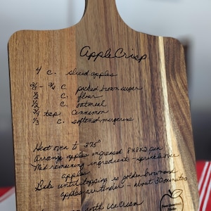 May include: A wooden cutting board with a recipe for Apple Crisp engraved on it. The recipe includes ingredients like sliced apples, packed brown sugar, flour, oatmeal, cinnamon, and softened margarine. The instructions are to heat the oven to 375 degrees Fahrenheit, arrange the apples in a greased 8x8 inch pan, sprinkle the remaining ingredients over the apples, and bake until the topping is golden brown and the apples are tender, about 30 minutes. Serve warm with ice cream.