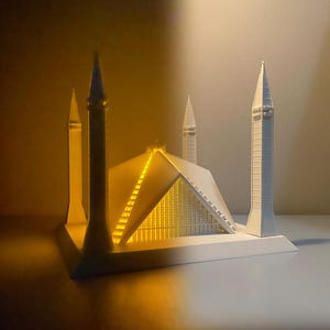 May include: A white 3D printed model of the Faisal Mosque in Islamabad, Pakistan. The model is lit from within, illuminating the interior of the mosque.