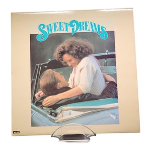 May include: Vintage vinyl record album cover titled "Sweet Dreams." The cover features a couple in a car, with the woman leaning over the man. The title is in turquoise script. The album is displayed on a clear stand.