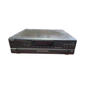 Op de afbeelding: Een zwarte Technics compact disc changer SL-PD8 met een digitale optische uitgang. Het apparaat heeft een display en tal van knoppen voor bediening. De tekst "4 Disc Rotary Changer System" is zichtbaar.