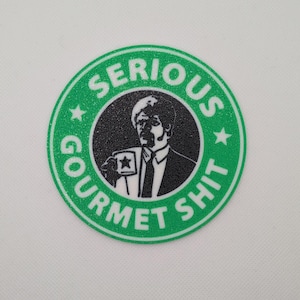May include: A green and black round sticker with the text "SERIOUS GOURMET SHIT" in white. The sticker features a black and white image of a man holding a cup with a star on it.