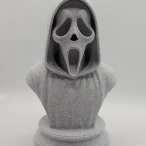 May include: A speckled gray bust of the Ghostface mask from the Scream horror film franchise. The bust features a hooded cloak and a screaming mask with large eye sockets and an open mouth.