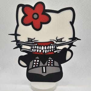 May include: A white Hello Kitty figurine with a red flower on its head. The figurine has a black and grey outfit and a red, toothy mouth.