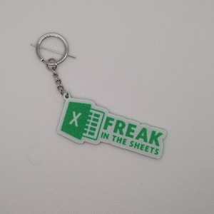 May include: A green and white keychain with the text "X FREAK IN THE SHEETS". The keychain has a silver-coloured ring and chain. The design features an Excel spreadsheet icon.