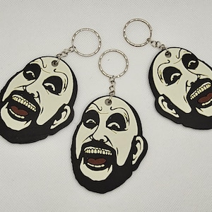 Könnte beinhalten: Drei schwarze und weiße Schlüsselanhänger aus Gummi mit einem Comic-Charakter mit Bart und breitem Lächeln. Jeder Schlüsselanhänger hat einen silbernen Metallring.