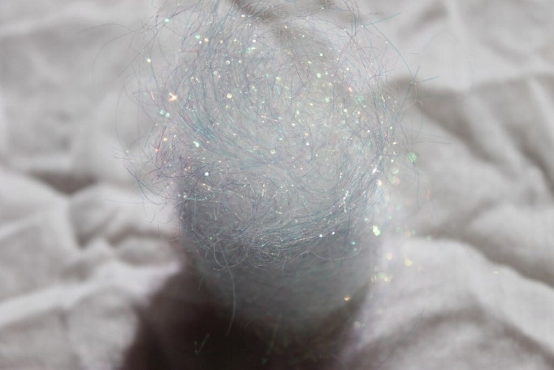 以下が含まれることがあります： 白くてふわふわした虹色の素材のクローズアップ。キラキラした質感です。この素材は、クラフトや装飾に使用される可能性があります。