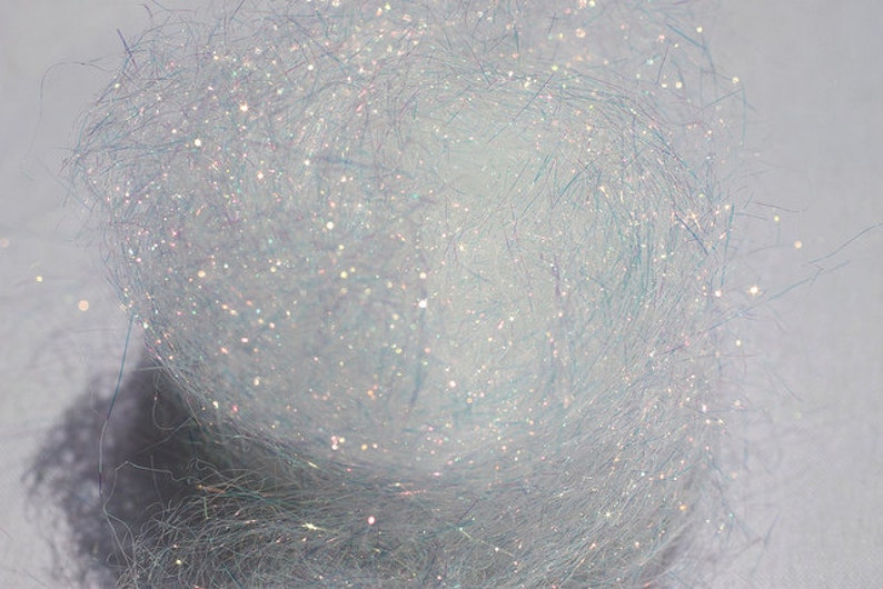 以下が含まれることがあります： 虹色の白いキラキラ糸のクローズアップ。糸は細かい繊維でできており、繊細でキラキラした外観をしています。