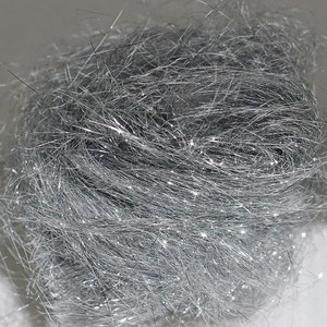May include: A close-up of a ball of silver metallic tinsel. The tinsel strands are tightly packed together, creating a dense, textured appearance. The metallic strands catch the light, creating a sparkling effect. The overall shape is round and compact.