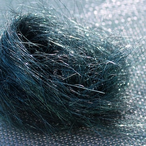 May include: A close-up of a teal blue sparkly yarn or thread, twisted into a ball shape. The yarn is soft and fluffy, with a subtle shimmer.
