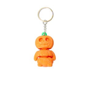 May include: Orange pumpkin-shaped keychain with a smiling face, a green stem, and a silver keyring. The pumpkin figure has a segmented body and arms. A fun Halloween accessory.