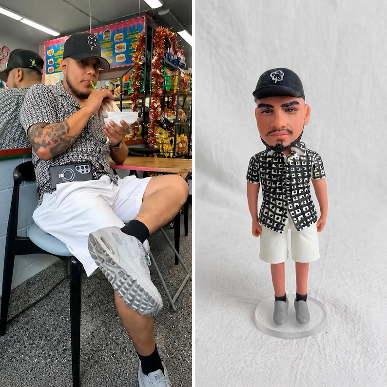 May include: A custom figurine depicting a person wearing a black baseball cap with a white clover logo, a black and white patterned short-sleeve button-down shirt, white shorts, black socks, and grey sneakers, standing on a clear circular base.