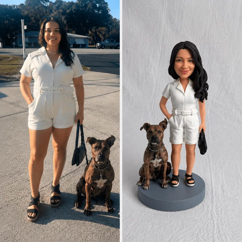 May include: A custom bobblehead figurine featuring a person with long dark hair wearing a white short-sleeved romper with a belt, black sandals, and carrying a small black handbag, standing next to a brindle dog on a round gray base.