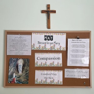 May include: A corkboard with various printed materials and a wooden cross. The board displays text including "Blessed Virgin Mary," "Compassion," and "Comfort/Visit the Sick." A picture of the Virgin Mary is also present.
