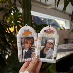 May include: Two white photo frames with rounded tops, each holding a photo of a person. The frames are decorated with cartoon food and characters. The text "Be Lucky Lucky" is printed on the bottom of one frame.