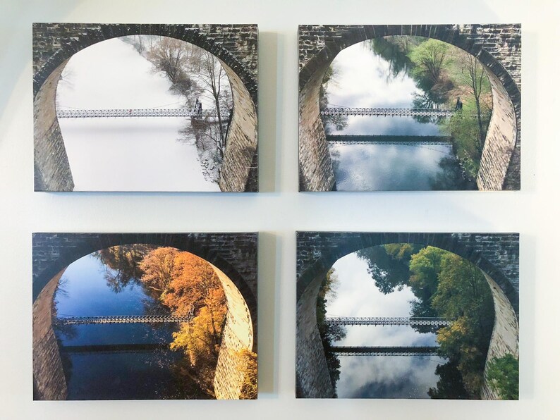 Pu&ograve; includere: Quattro stampe rettangolari su tela disposte a griglia. Ogni stampa presenta un arco in pietra che incornicia la vista di un ponte sospeso su un fiume, mostrando lo stesso paesaggio durante le quattro diverse stagioni dell'anno.