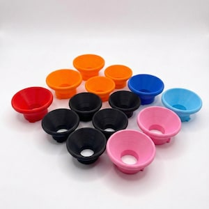 May include: A collection of fourteen small, funnel-shaped plastic objects arranged in a grid. The items are colored in red, orange, black, blue, light blue, and pink. Each piece features a wide, circular opening at the top and a narrow base.