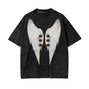 Op de afbeelding: Zwart T-shirt met een distressed look met een witte afbeelding van engelenvleugels met meerdere ogen op de rug.