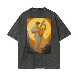 Op de afbeelding: Een zwart T-shirt met een vintage wassing met een print van een figuur die harp speelt voor een grote zon.