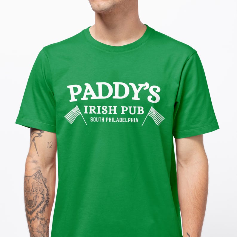 Puede incluir: Camiseta verde con texto blanco que dice "Paddy's Irish Pub South Philadelphia" y dos banderas americanas blancas.