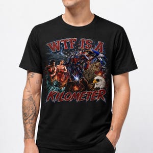 May include: A black short-sleeve t-shirt featuring a graphic print with the text "WTF IS A KILOMETER" in red. The design includes a collage of American cultural icons, including a bald eagle, the Statue of Liberty, and a T-Rex, set against a flag.
