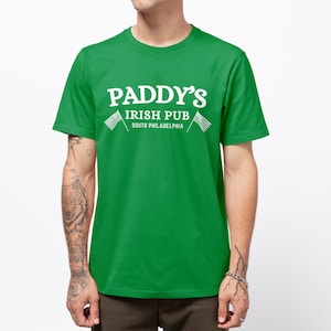 Puede incluir: Camiseta verde con texto blanco que dice "Paddy's Irish Pub South Philadelphia" con dos banderas americanas a cada lado del texto.