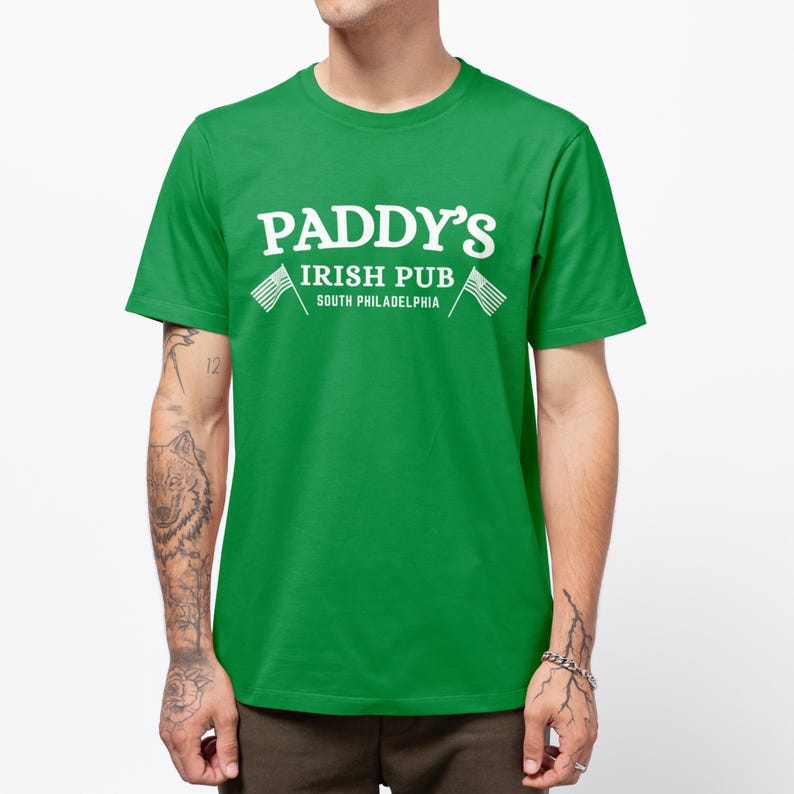 Puede incluir: Camiseta verde con texto blanco que dice "Paddy's Irish Pub South Philadelphia" con dos banderas americanas a cada lado del texto.