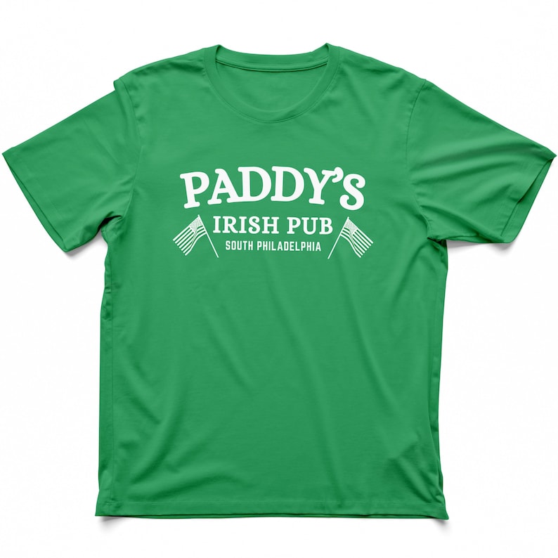 Puede incluir: Camiseta verde con texto blanco que dice "Paddy's Irish Pub South Philadelphia" con dos peque&ntilde;as banderas americanas a cada lado del texto.