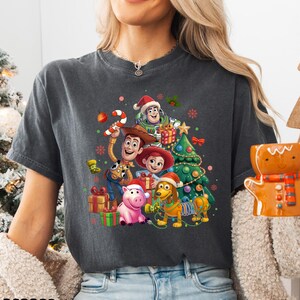 A woman wearing a gray t-shirt with a graphic design featuring characters from the Toy Story movie, including Woody, Buzz Lightyear, and other beloved characters.