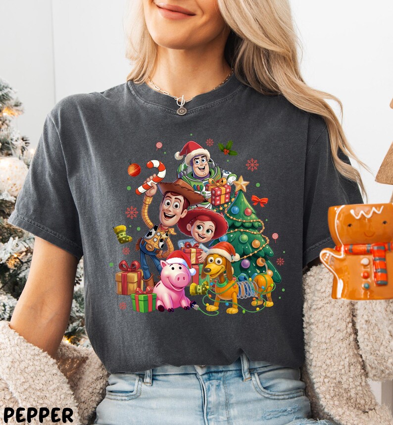 A woman wearing a gray t-shirt with a graphic design featuring characters from the Toy Story movie, including Woody, Buzz Lightyear, and other beloved characters.